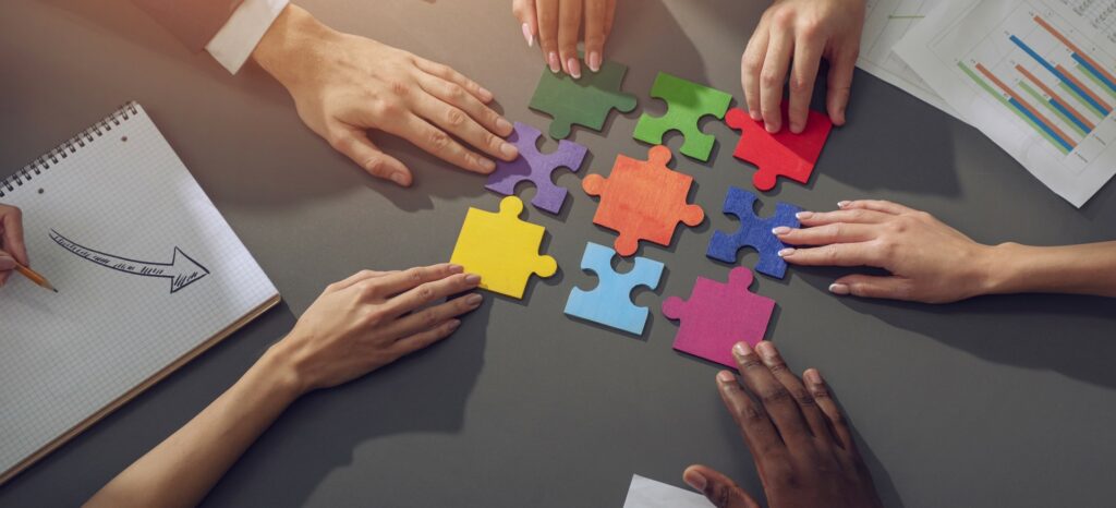 Several hands working together to complete a colourful jigsaw puzzle